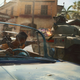 A soldier drives a convertible and tosses a grenade at a tank in Far Cry 6.